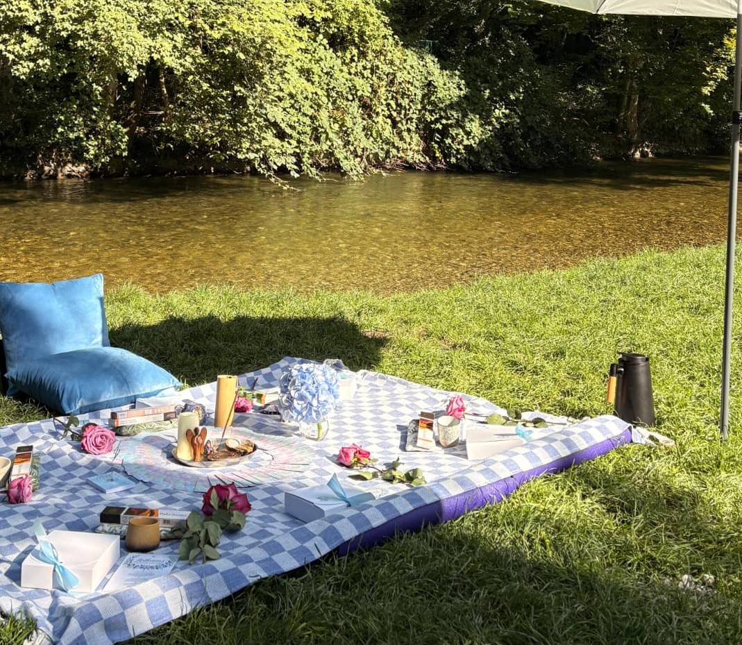 Mama Blessing picnic setup by the river with cushions, flowers and keepsake boxes